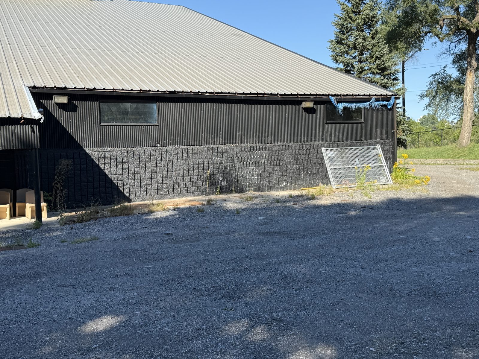 The existing block building today: dark painted block walls under a pitched metal roof, on a gravel lot