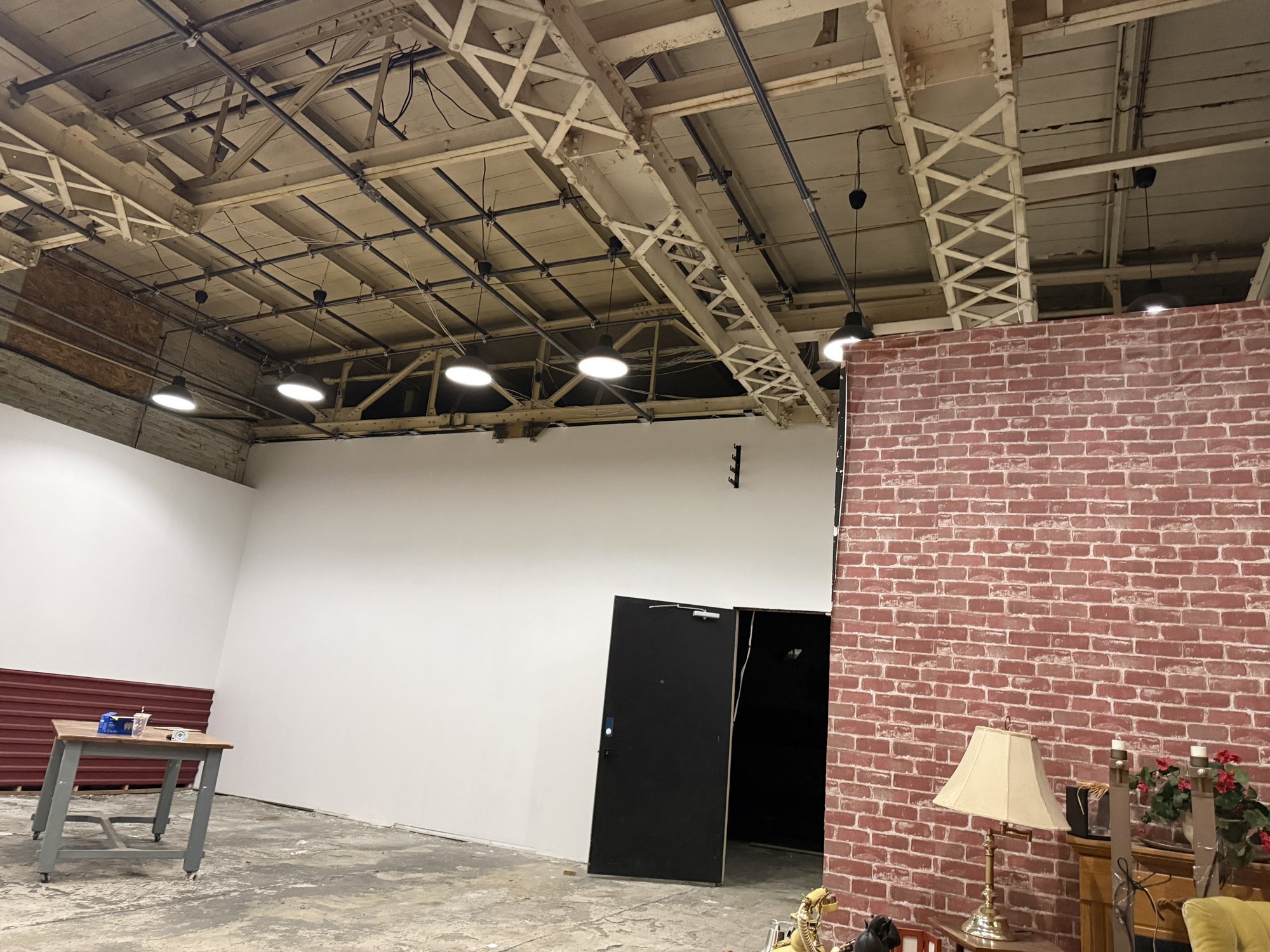 Studio floor at 252 Stuart Street — open trusses with lighting above the beams, a white wall and a brick flat